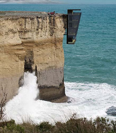 a view of cliff house above open water, hanging off the cliff's edge