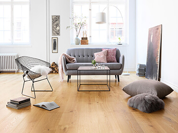 the Scandinavian interior design in a room uses a Sled base steel chair, a steel table and a gray sofa on the wooden flooring