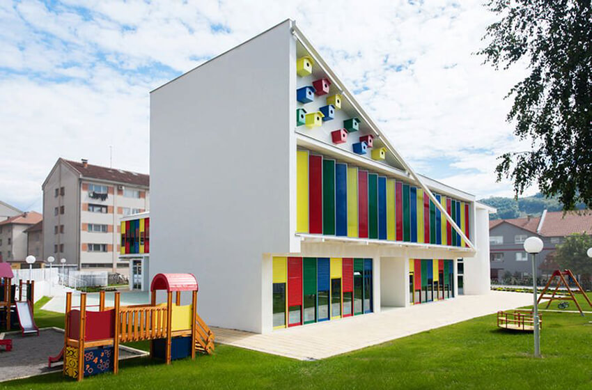 a green playground and a kindergarten building with a colorful facade