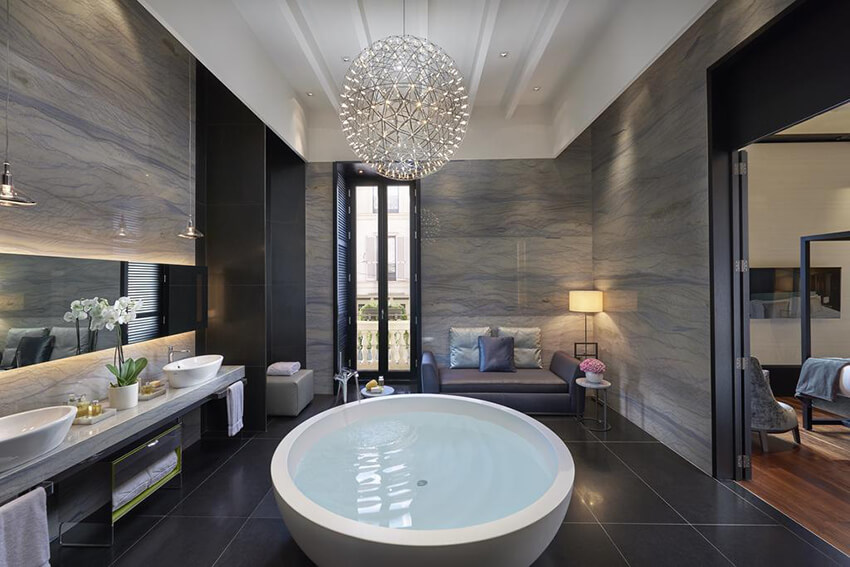 a hotel bathroom with black stone flooring tiles, a white bathtub, and perfect lighting